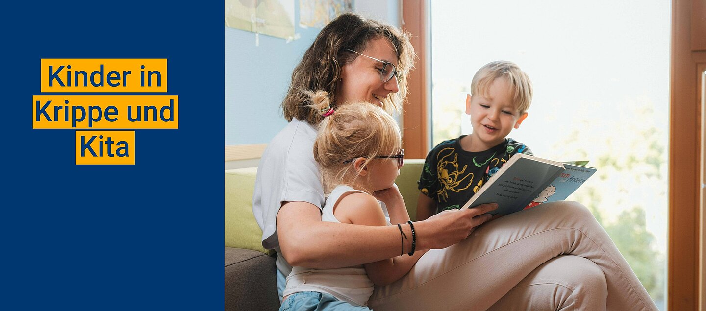 Zwei Kindern wird von einer Kitafachkraft vorgelesen