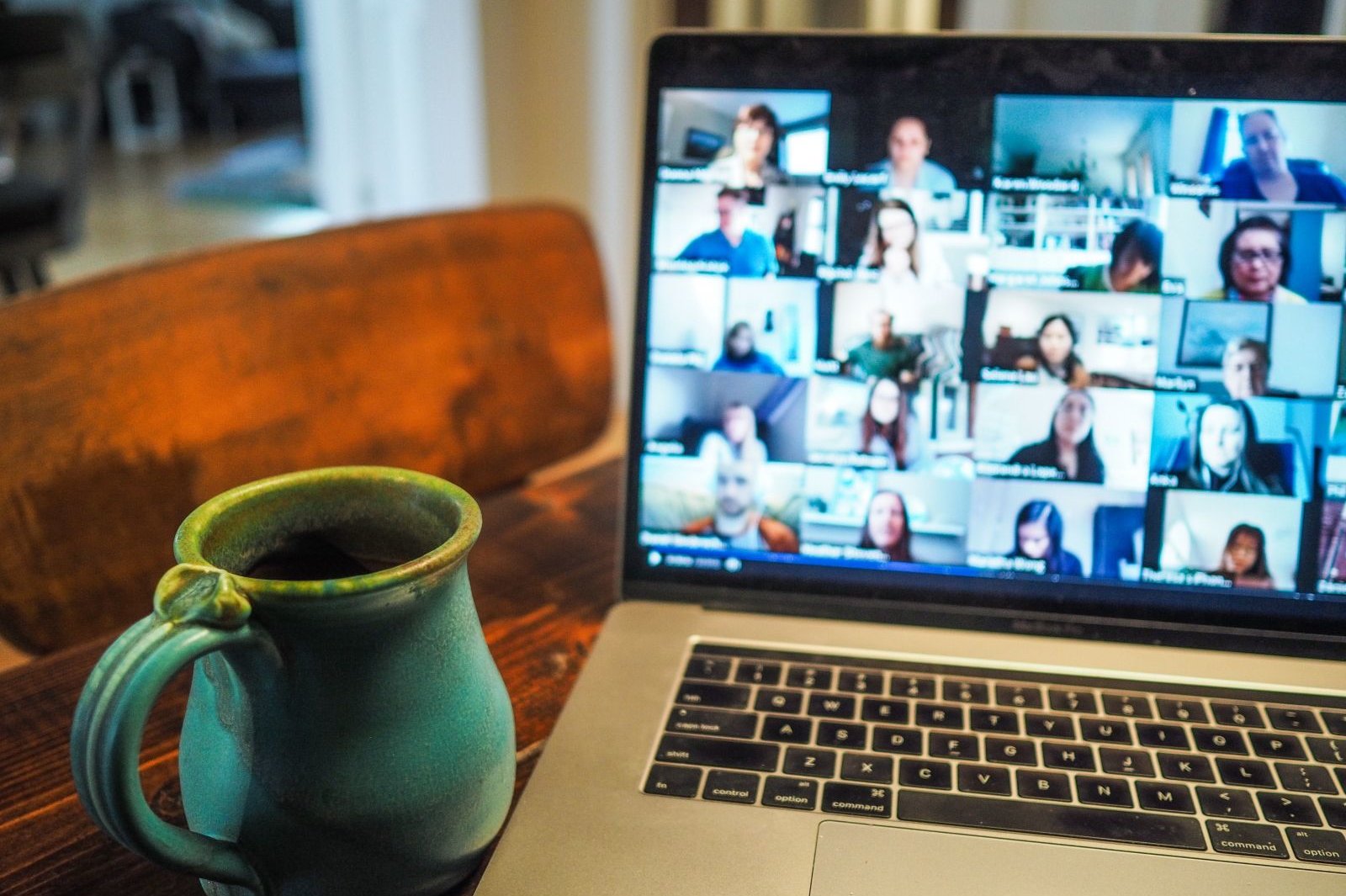 Laptop mit Abbildung einer Videokonferenz mit zahlreichen Teilnehmenden; daneben eine Kaffeetasse