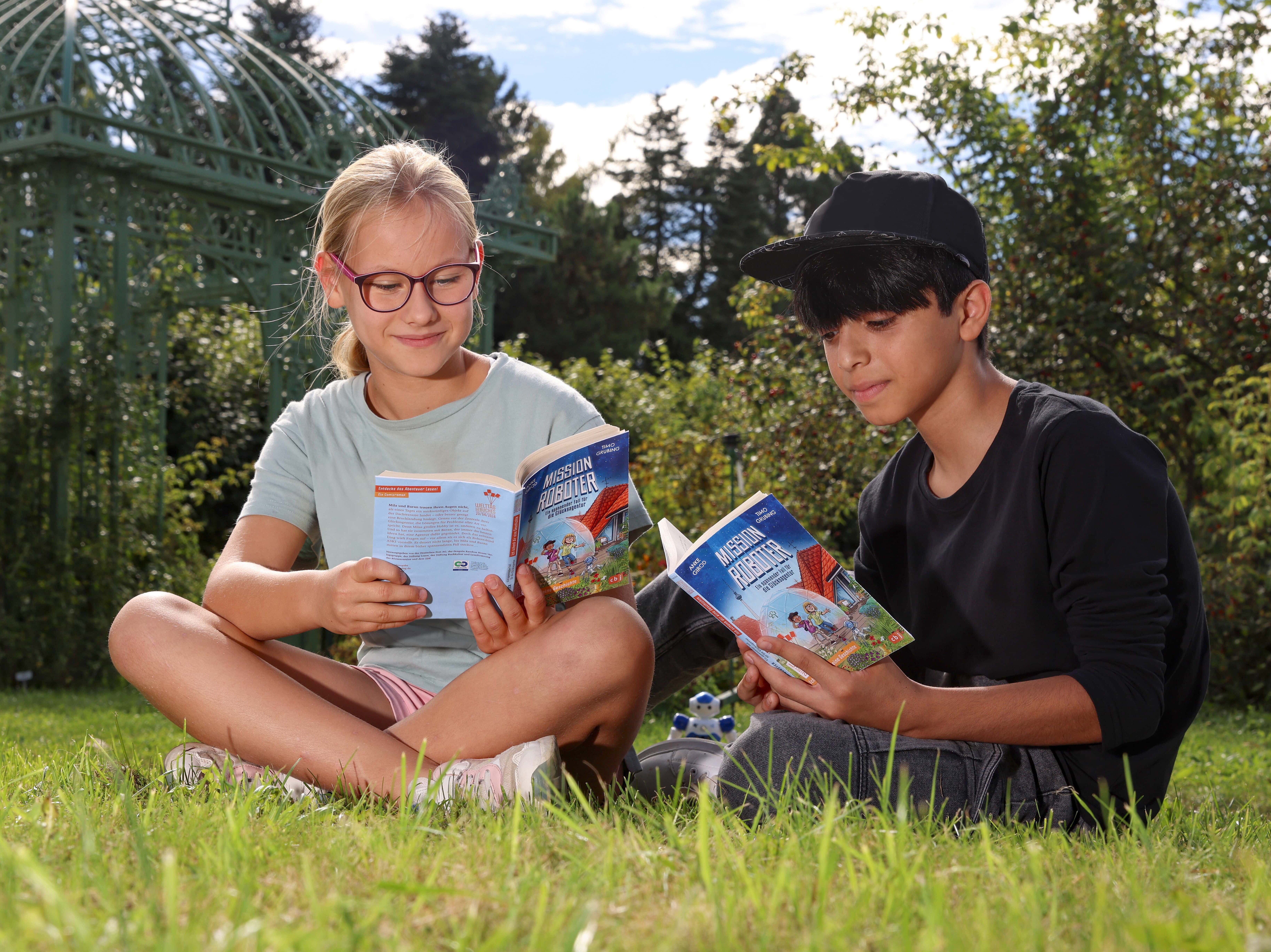 Ein Junge und ein Mädchen sitzen auf einer Wiese und schauen in ein Buch