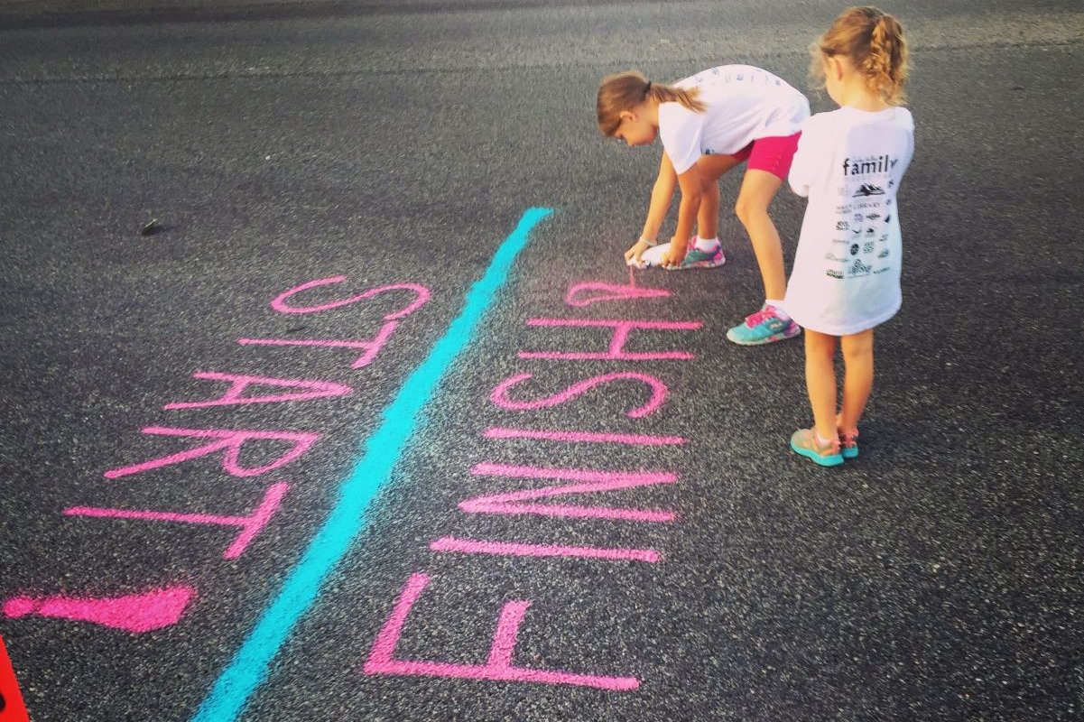 Zwei Mädchen zeichnen mit Kreide eine Start-Ziel-Linie auf die Straße
