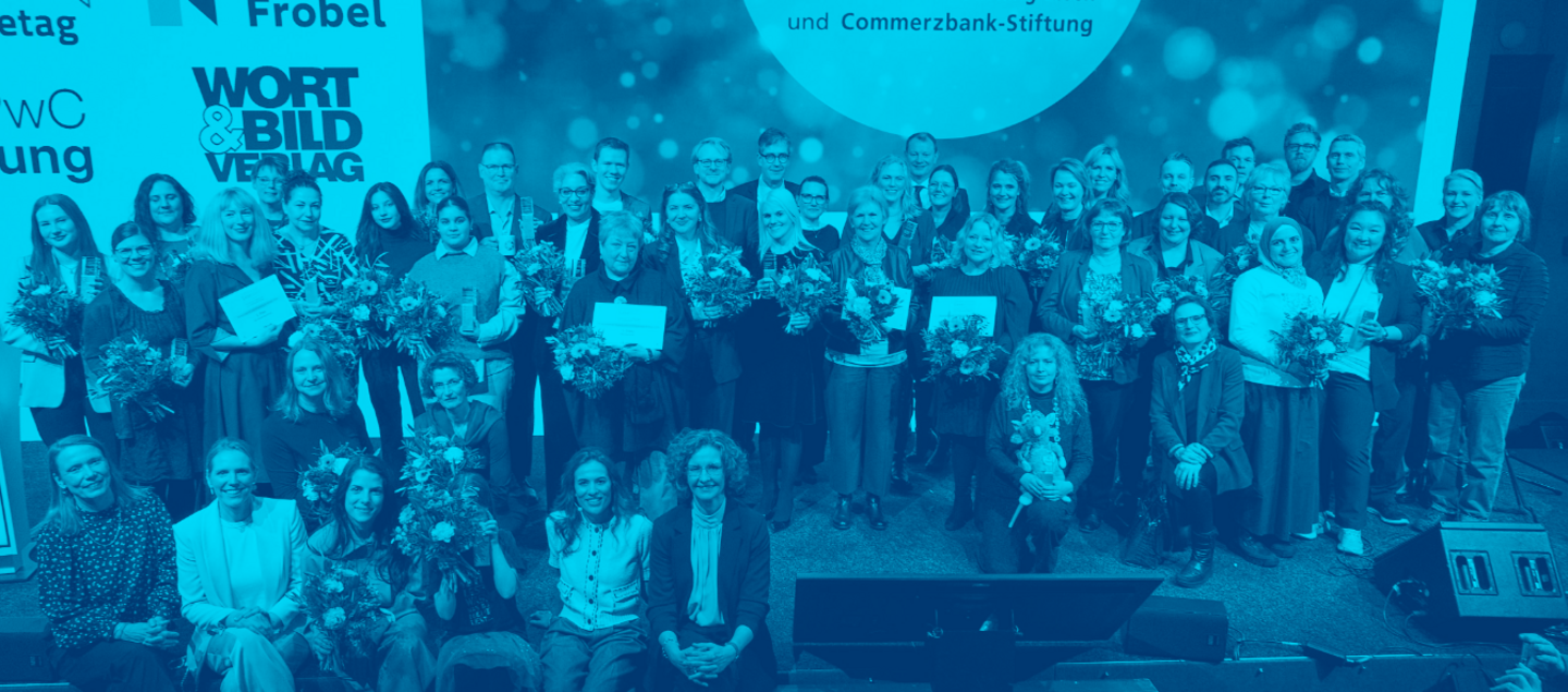 Große Gruppe von Preisträger*innen steht gemeinsam auf einer Bühne beim Deutschen Lesepreis, viele halten Blumensträuße und Urkunden in den Händen; im Hintergrund ist eine Veranstaltungswand mit dem Schriftzug „Deutscher Lesepreis“ zu sehen.