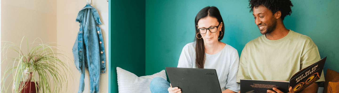 Eine Frau schaut auf einen Laptop und ein Mann in eine Buch 