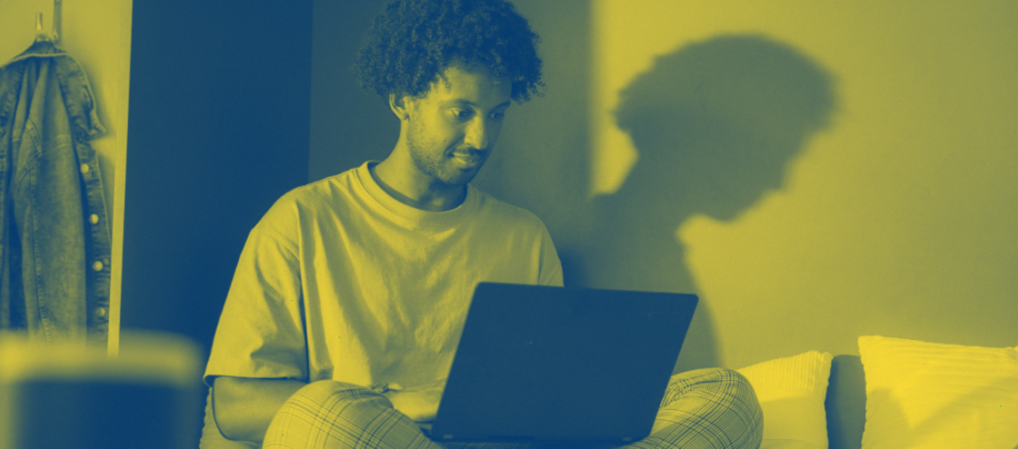 Gelb eingefärbtes Foto eines jungen Mannes, der auf einem Sofa sitzt und auf einem Laptop arbeitet.